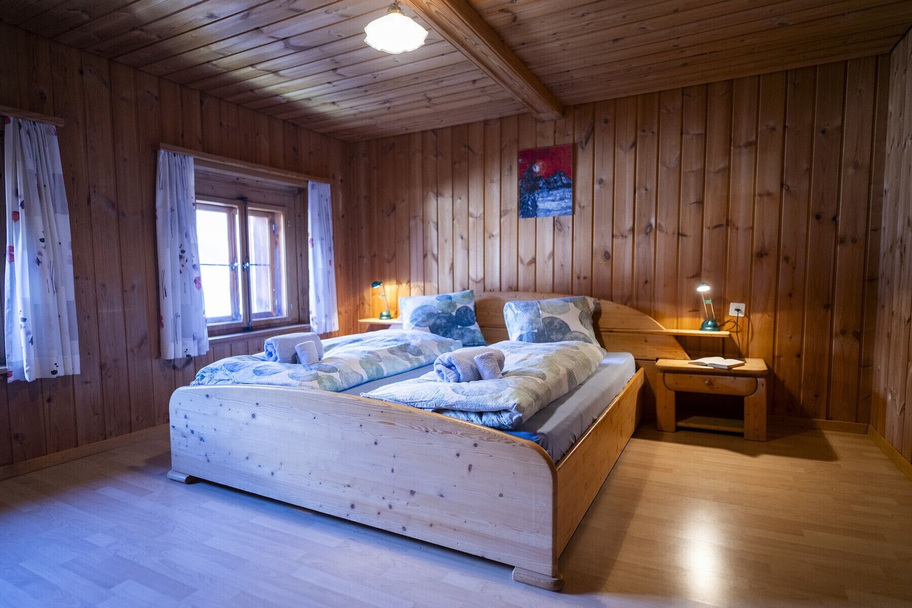 Un dormitorio con paneles de madera, una cama, dos mesitas de noche y una ventana con cortinas.