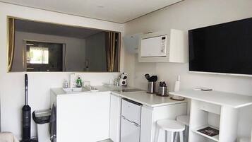 Cocina compacta con microondas, pileta y taburetes de bar.