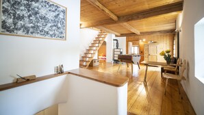 A spacious room with wooden floors, a dining table, a sofa, and a staircase leading to another level. - Chasa Riatsch: Renovated Engadine house in the centre of Ardez (Ardez)