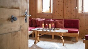 A wooden room with a red sofa, a round wooden table with candles, and a window with curtains. - Chasa Riatsch: Renovated Engadine house in the centre of Ardez (Ardez)