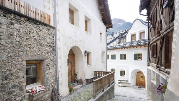 A narrow cobblestone street flanked by traditional buildings with stone walls and wooden balconies. - Chasa Riatsch: Renovated Engadine house in the centre of Ardez (Ardez)