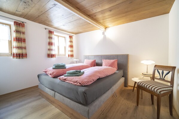 A bedroom with a bed, a chair, a table, and a window with curtains.