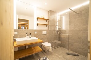 A modern bathroom with a glass shower enclosure, a wooden vanity, and a toilet.