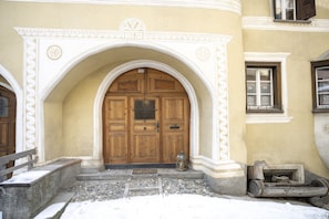 A building entrance with a wooden door, an arched doorway, and a small lantern on the steps.