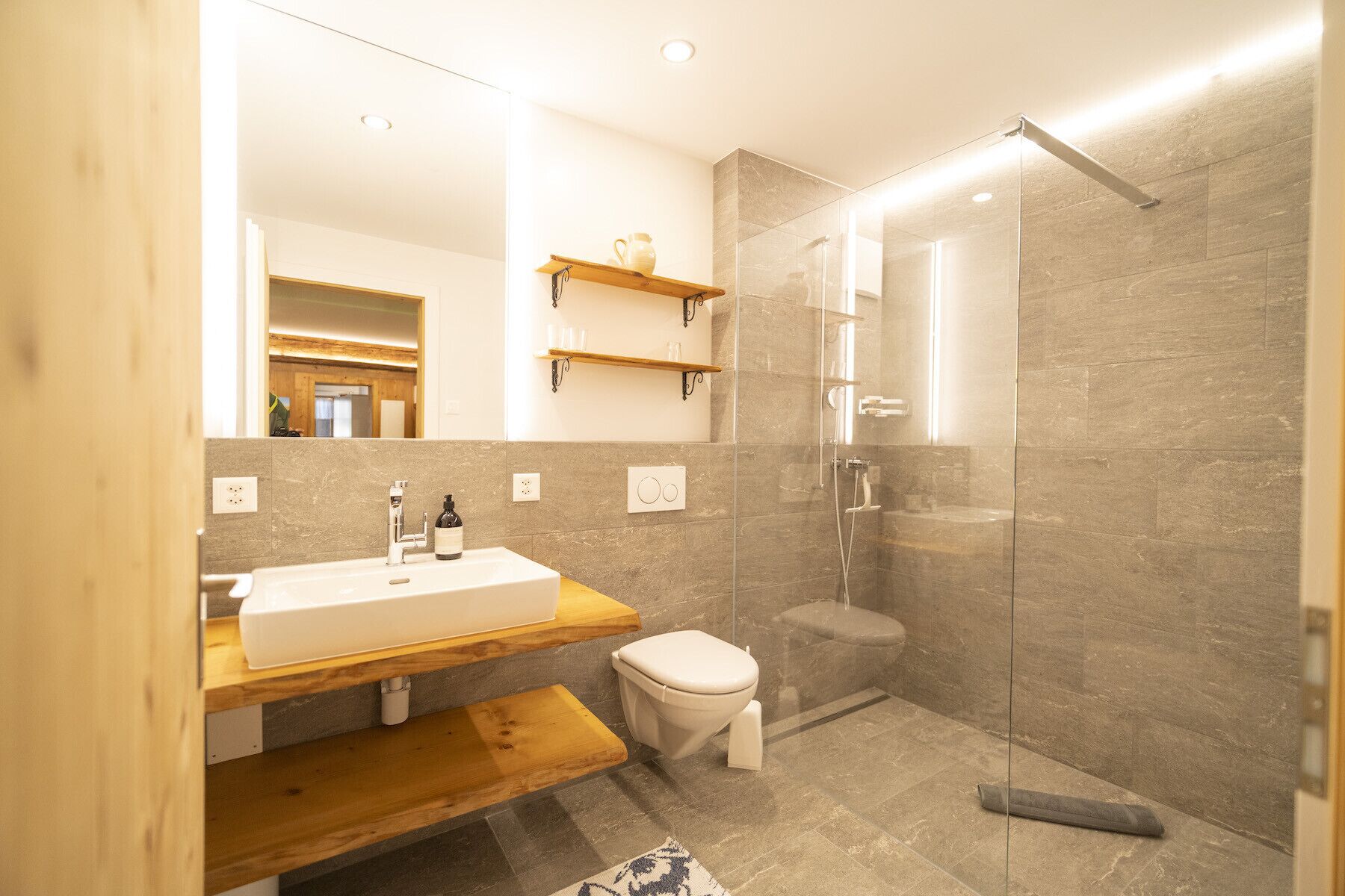 Une salle de bain moderne avec un meuble-lavabo en bois, des toilettes et une douche à parois de verre.