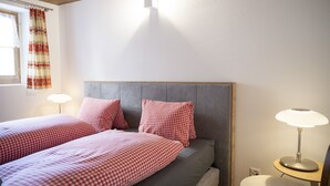Une chambre avec deux lits, une tête de lit grise et une table de chevet avec une lampe.