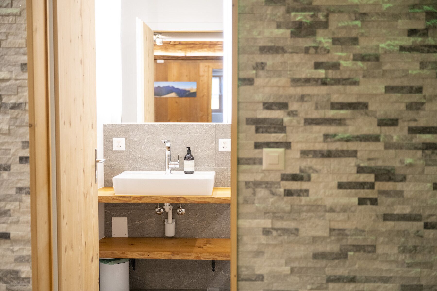 A modern bathroom with a wooden vanity, a white sink, and a mirror.