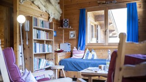 Een gezellig houten interieur met een boekenkast, een bed met blauw beddengoed en een kleine tafel.