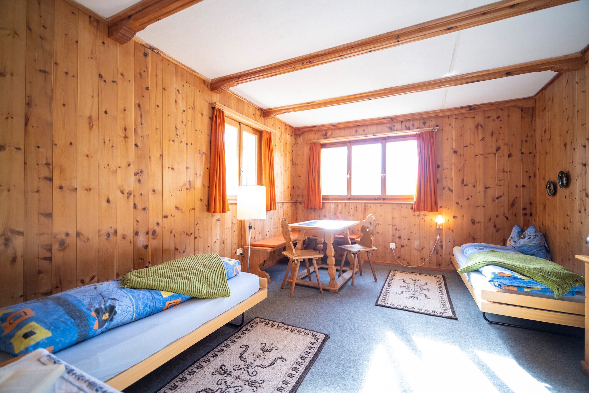 A wooden cabin room with two beds, a table, chairs, and a window.