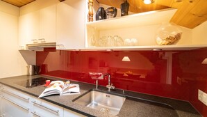 Een moderne keuken met een granieten aanrecht, een roestvrijstalen spoelbak en een rode achterwand.