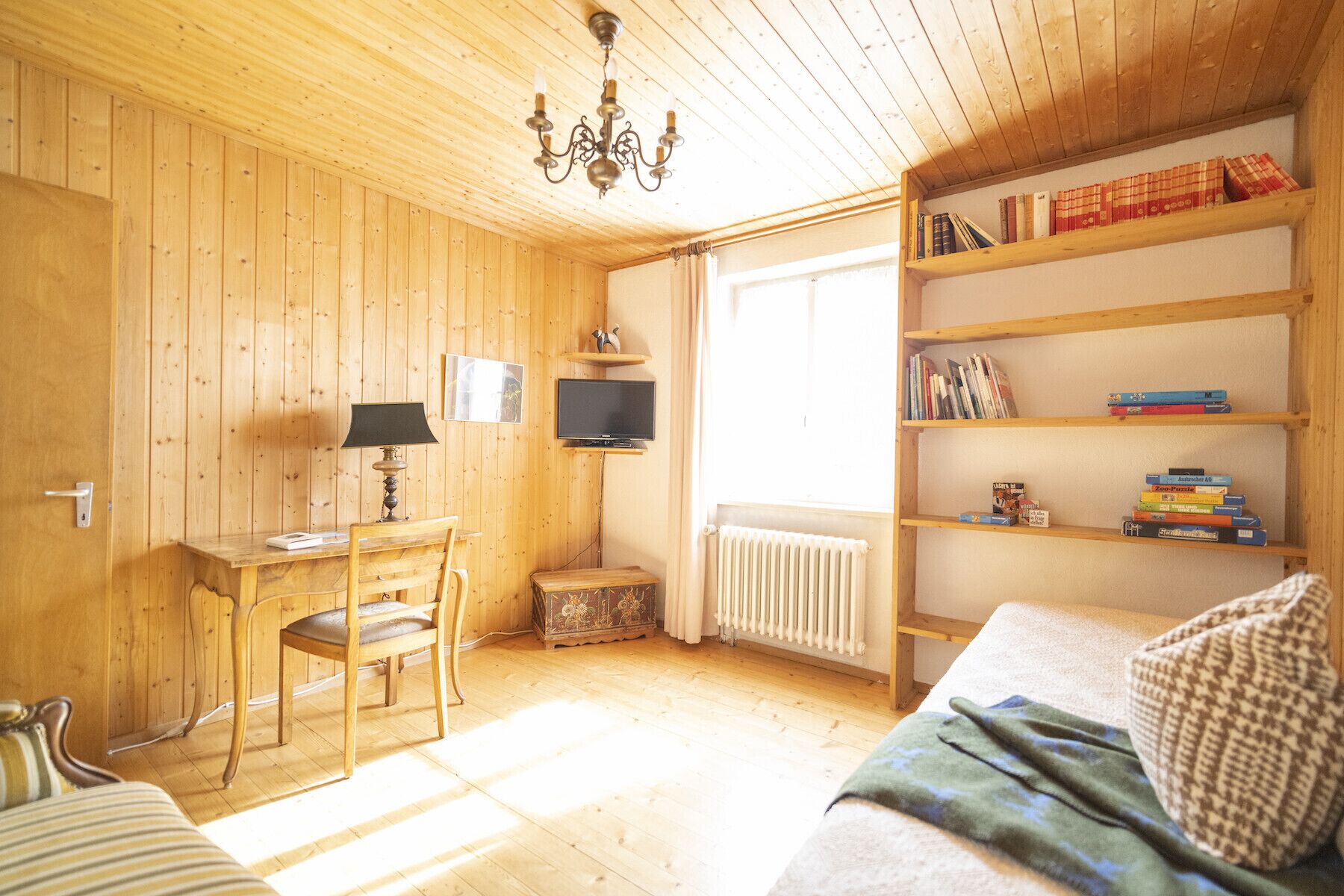 Una habitación acogedora con paredes y suelos de madera, un escritorio con lámpara, un televisor, una estantería y un radiador.
