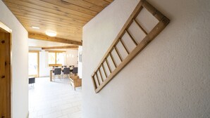 Un couloir avec des poutres en bois au plafond, un mur blanc orné d’une lambris en bois, et un coin repas à l’arrière-plan.
