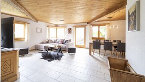 Un vaste espace de vie doté d’un haut plafond en bois, d’un ensemble de canapés, d’une table à manger avec des chaises et d’un téléviseur.
