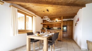 Un coin repas avec une table et des chaises en bois, une cuisine à l’arrière-plan et un plafond en bois.