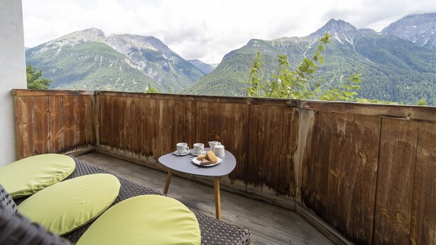 Un balcon agrémenté de meubles en osier et d’une petite table avec des tasses et des biscuits, offrant une vue sur un paysage montagneux.