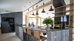 Una cuina moderna amb una illa central, tamborets de bar, il·luminació penjant i electrodomèstics integrats.