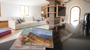Revista damunt d'un taulell en una habitació amb un sofà blanc, prestatges de fusta i una màquina de cafè.