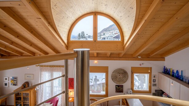 Ein Zimmer mit hohen Decken und einem großen Bogenfenster mit Blick auf eine verschneite Landschaft.
