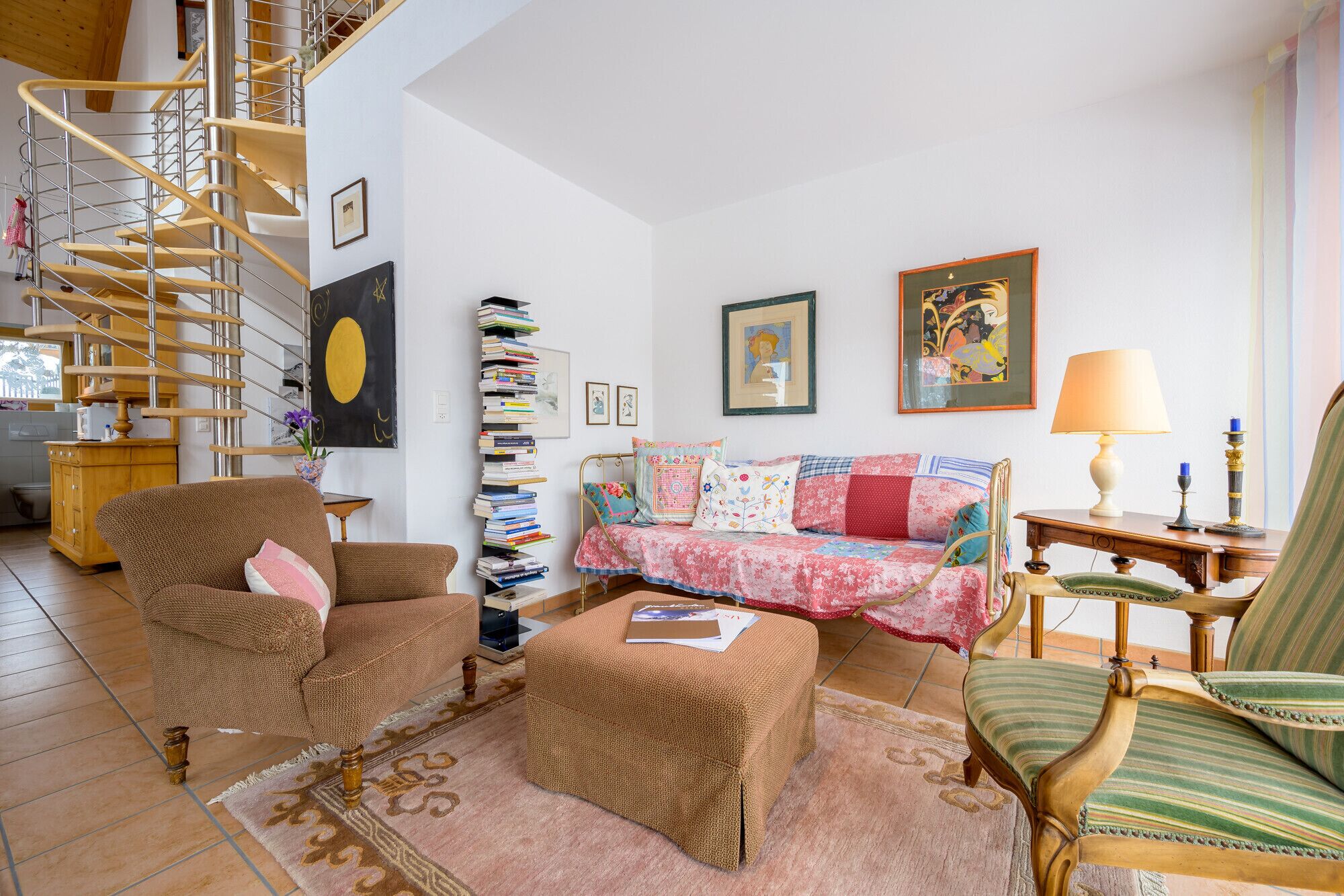 A cozy living room with a spiral staircase, a sofa set, a bookshelf, and a lamp.
