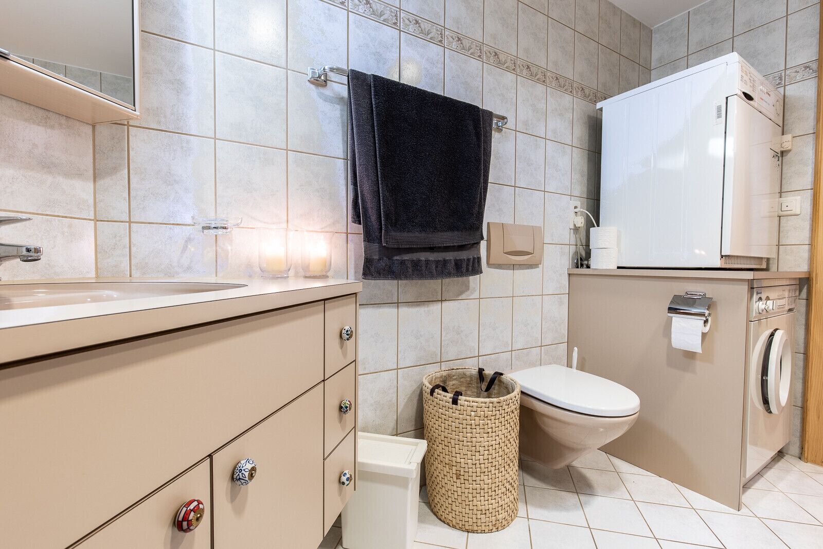 A bathroom with a toilet, washing machine, and a sink with a mirror above it.