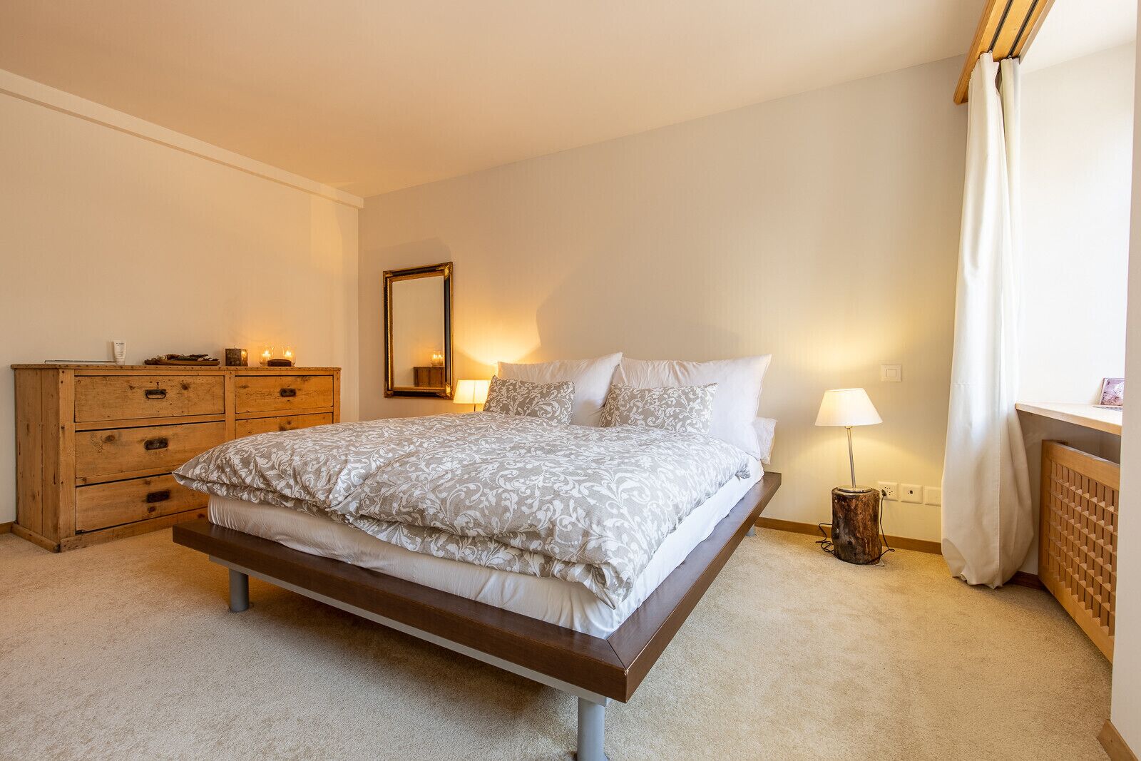 Ein Schlafzimmer mit einem Bett, einer Holzkommode, Nachttischlampen und einem Spiegel.