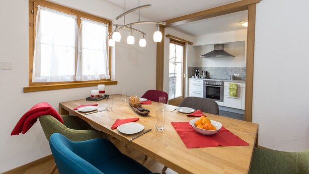 A dining area with a wooden table, chairs, and a view into the kitchen.