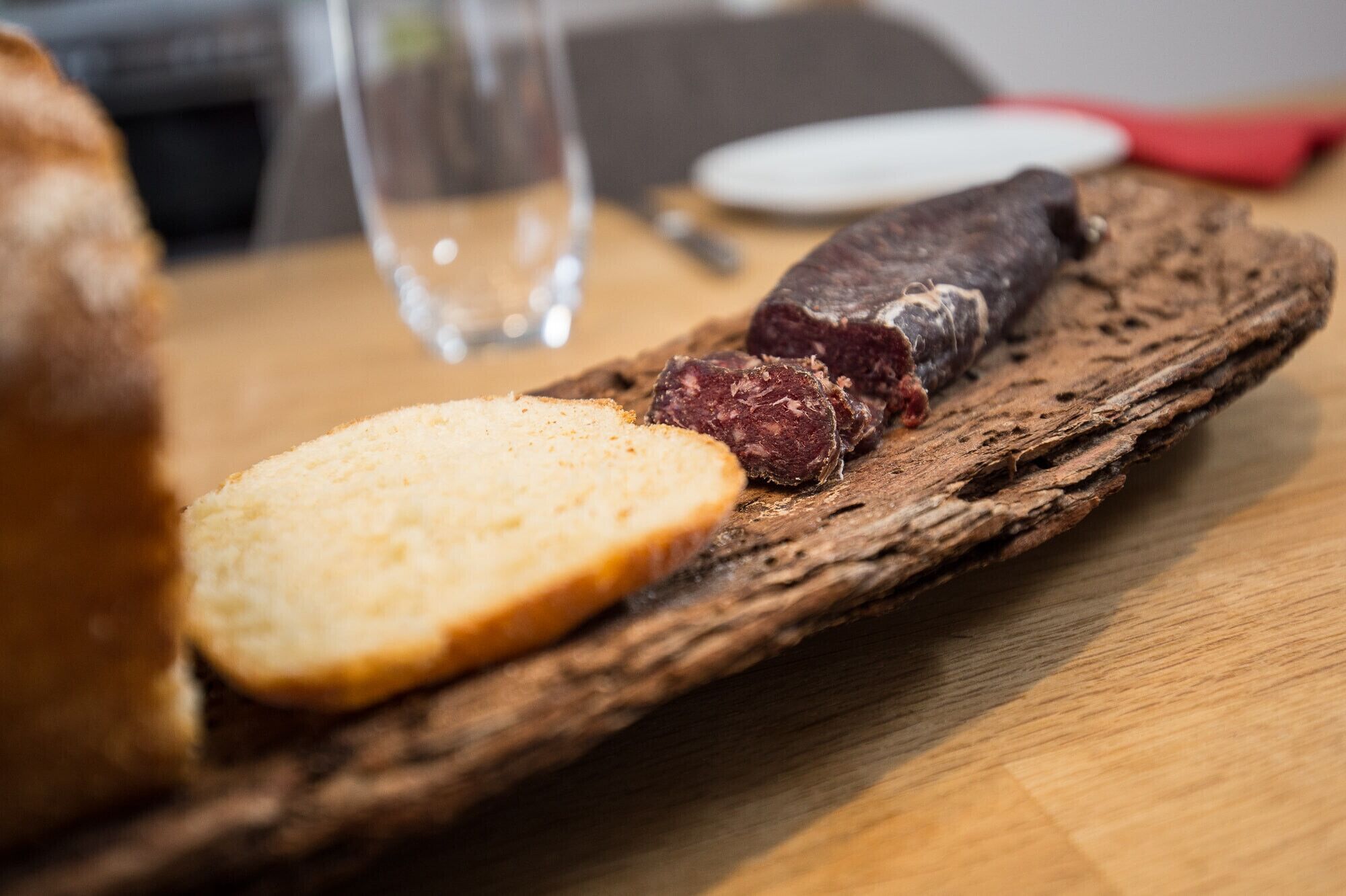 A wooden serving board with a slice of bread and a piece of cured meat.