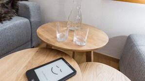 A small wooden table with two glasses and a bottle, a tablet on the table, and grey sofas in the background.