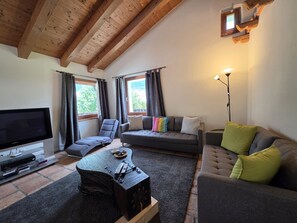 Ein Wohnzimmer mit Fernseher, Sofas, einem Couchtisch und einer Holzbalkendecke.