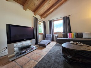 A living room with a flat-screen TV, a grey sofa, a small ottoman, and a coffee table.