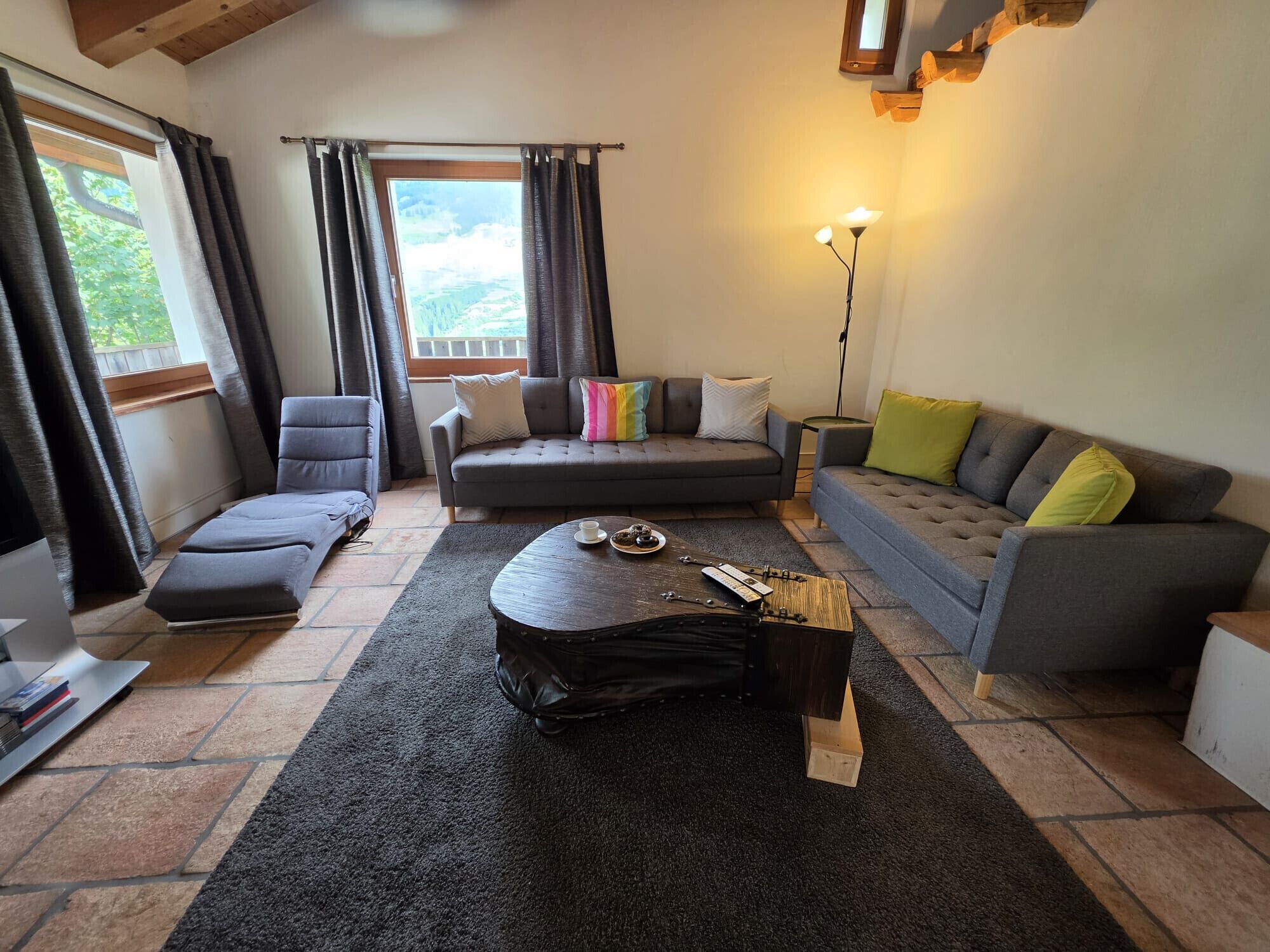 Una sala de estar con sofá, sillón y una mesa de centro, una lámpara y vistas por la ventana.