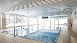 Sisätiloissa sijaitseva uima-allas, jonka seinät ovat kirkasta lasia, lattia on laatoitettu ja katossa on vaakasuora kuvio.