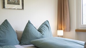 Hotellihuone, jossa on sänky, tyynyjä, lamppu ja ikkuna, jossa on verhot.