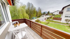 A balcony with a wooden railing, a white table, and two white chairs. There are bottles and a glass on the table. - Chasa Trü No. 7: Trü holiday settlement- Apartment No. 7 (Scuol)