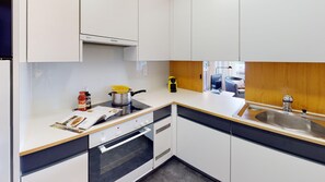 Eine moderne Küche mit weißen Schränken, einem Herd, einem Backofen, einer Spüle und einem Fenster mit Blick nach draußen.