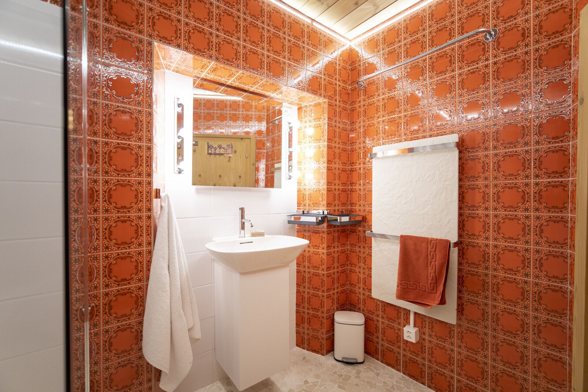 Un baño con baldosas anaranjadas con diseño, un lavamanos blanco, un espejo y un perchero para toallas.