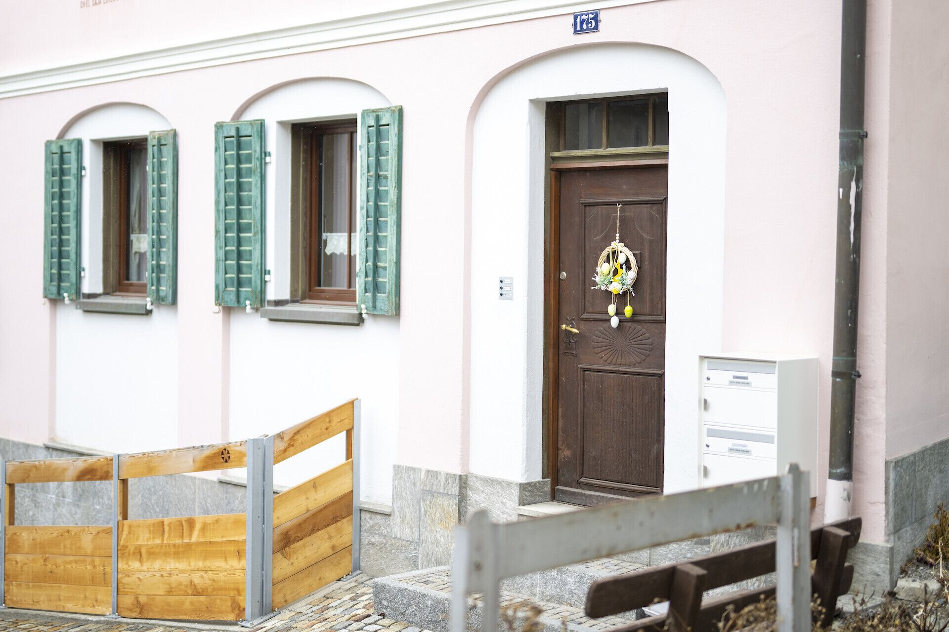 Un bâtiment doté d’un portail en bois, d’une porte marron ornée d’un élément décoratif suspendu et d’une boîte aux lettres.