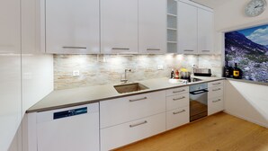 A modern kitchen with white cabinets, a stainless steel sink, and a built-in oven. - Chasa Vista Pisoc: Modern 2 ½-room apartment in the centre with panoramic views (Scuol)
