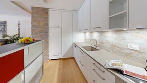 A modern kitchen with white cabinets, a stone accent wall, and a wooden floor. - Chasa Vista Pisoc: Modern 2 ½-room apartment in the centre with panoramic views (Scuol)