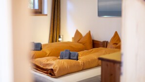 A neatly made bed with a brown comforter and pillows, a small bedside table, and a window with curtains. - Chasa Val 735C: Quiet, cozy 3 ½-room apartment with fireplace and panoramic views of the national park (Scuol)