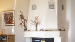 A modern living room with a white fireplace, a wooden ceiling, and a framed artwork on the wall. - Chasa Val 735C: Quiet, cozy 3 ½-room apartment with fireplace and panoramic views of the national park (Scuol)