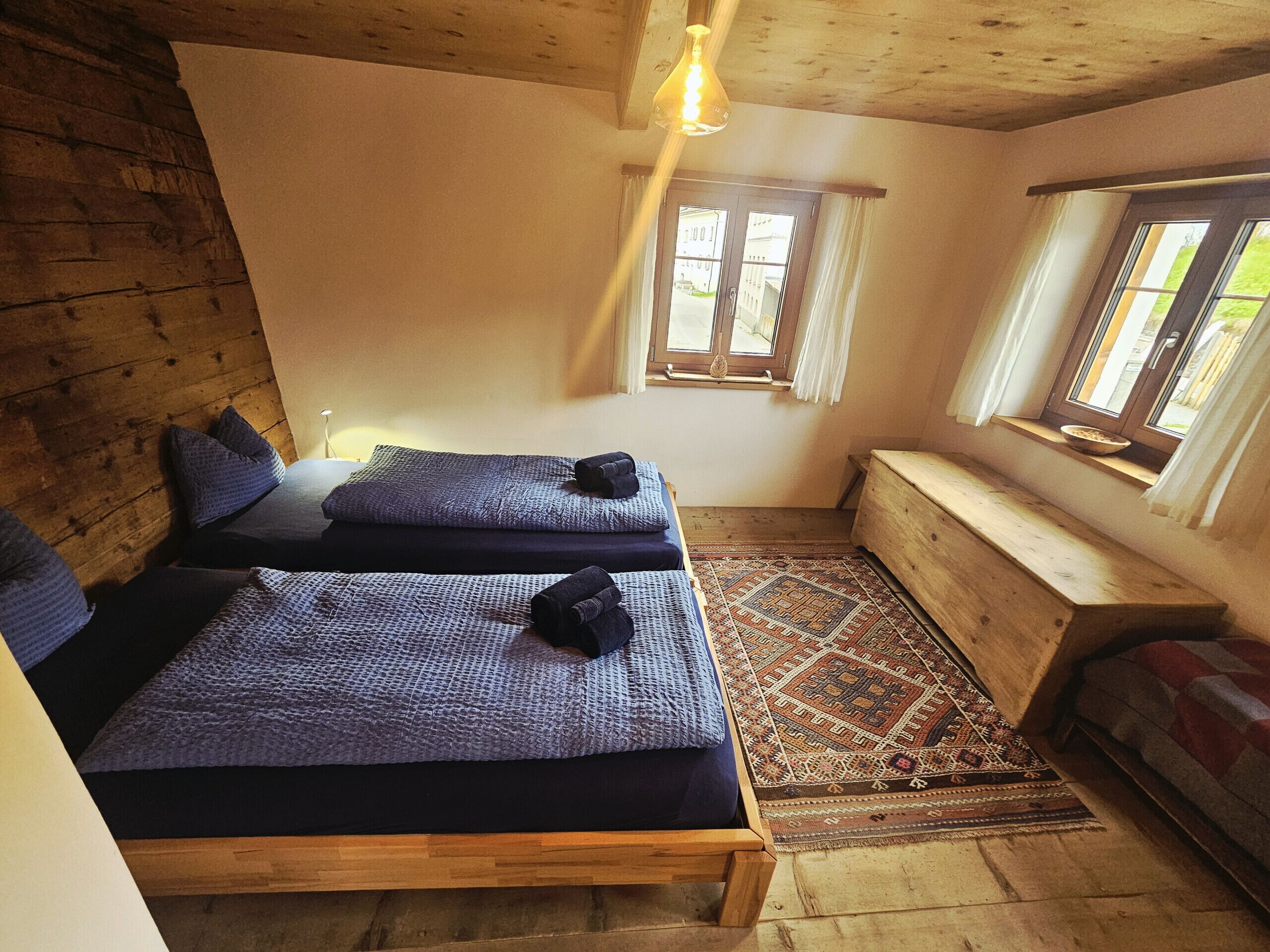 A cozy room with two beds, a bench, and a view of the street through a window.