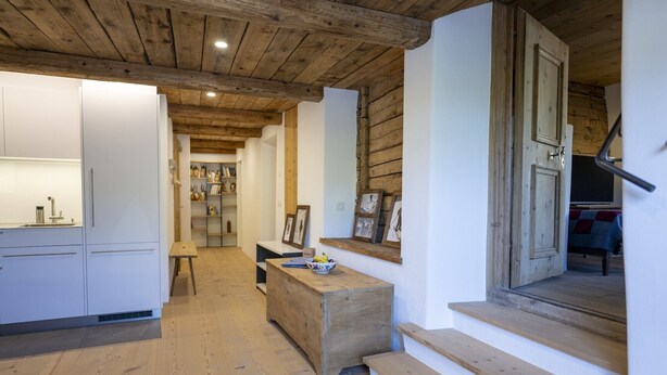 A rustic interior with wooden beams, a kitchen area, and a staircase leading to another level. - Chasa Bijou: Idyllic 3-room apartment in the quiet mountain village of Ftan (Ftan)