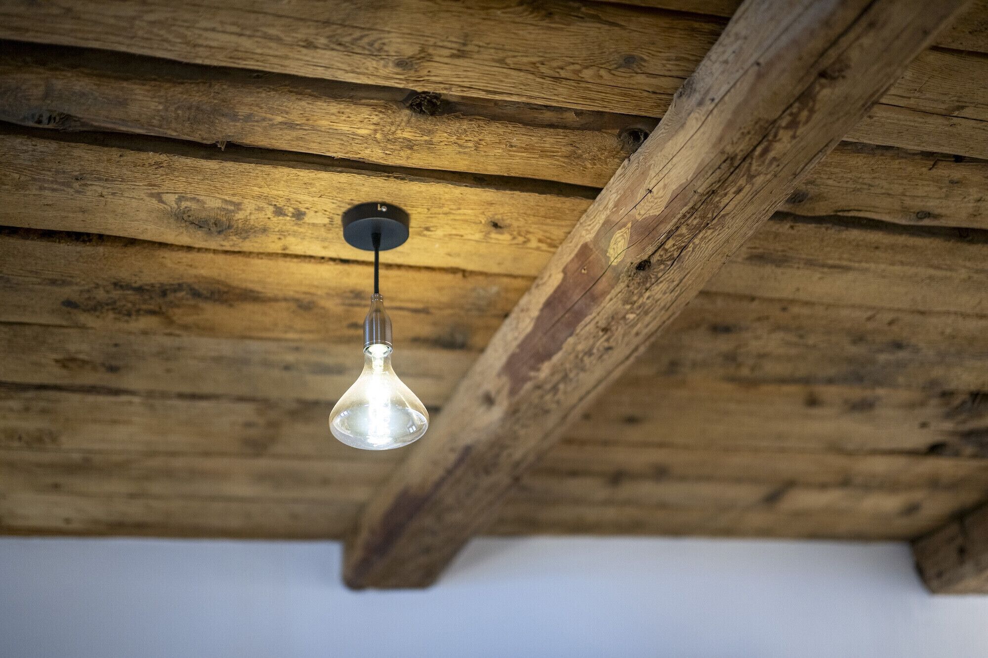 Un plafond avec des poutres apparentes et une seule suspension lumineuse.