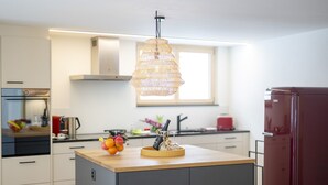Una cocina con una isla central, una lámpara colgante, un refrigerador y un ventanal.