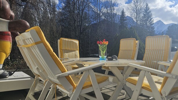Un tavolo con quattro sedie a righe, un vaso con fiori e una vista panoramica sulle montagne sullo sfondo.