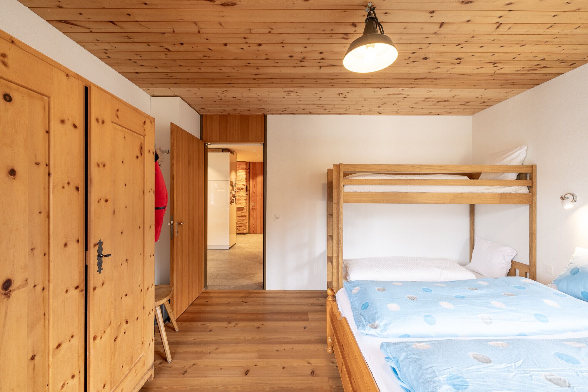 Une chambre avec un lit superposé en bois, un plafond en bois et un luminaire.