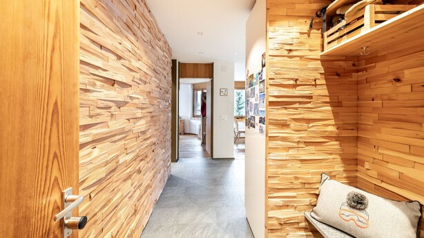 A hallway with wooden panel walls, a bench with a cushion, and a door with a handle.