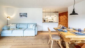 A modern living room with a light blue sofa, a wooden dining table with chairs, and a kitchen in the background.