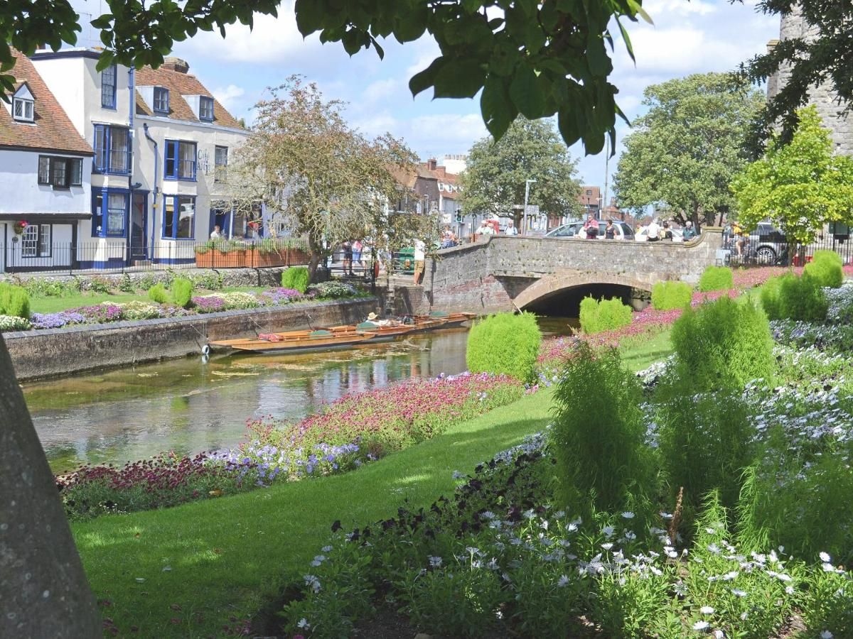 Un jardin au bord de la rivière, agrémenté d’un pont, d’une végétation luxuriante et d’un bâtiment historique.
